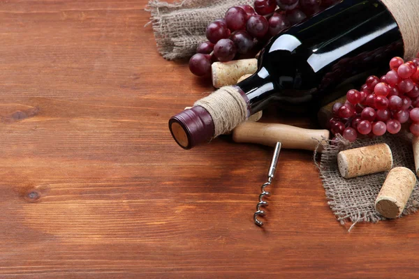 Botella de vino, uvas y corchos sobre fondo de madera — Foto de Stock