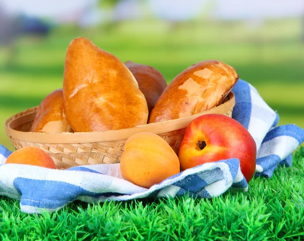 Frisch gebackenes Gebäck mit Früchten, im Weidenkorb, auf Gras, auf hellem Hintergrund — Stockfoto