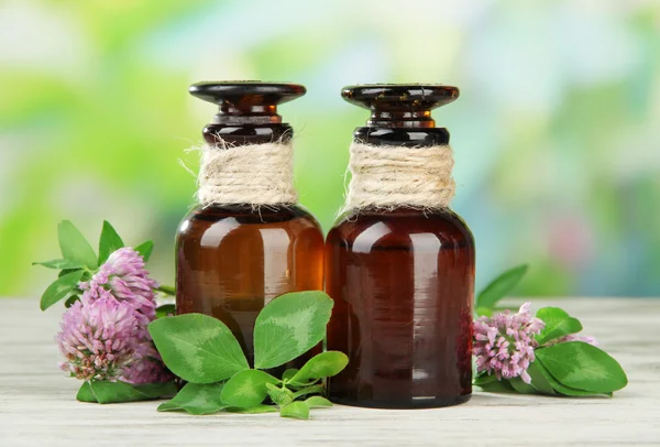 Medicine bottles with clover flowers on wooden table, outdoors — Stock Photo, Image