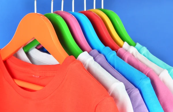 Különböző ingek a kék háttér színes fogasok — Stock Fotó