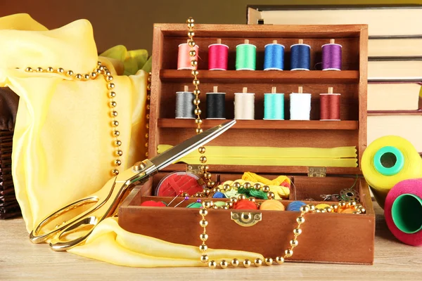 Kit de costura en caja de madera con libros y mesa de tela sobre fondo brillante — Foto de Stock