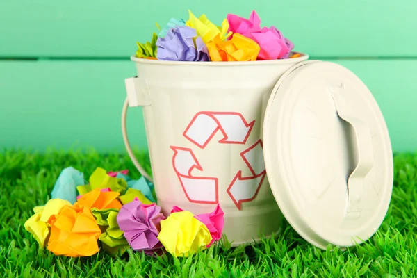 Recycling bin on green grass on color wooden background — Stock Photo, Image