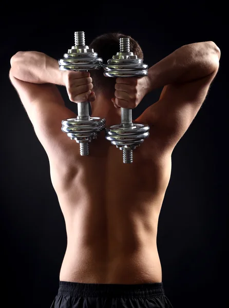 Handsome young muscular sportsman execute exercise with dumbbells on dark background — Stock Photo, Image