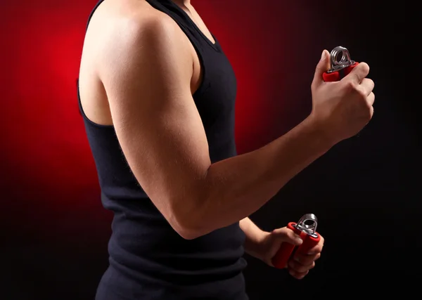 Handsome young muscular sportsman with expanders, on dark background — Stock Photo, Image