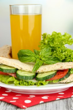 Lezzetli sandviç salam sosis ve parlak zemin üzerine ahşap masa üzerinde renkli peçete üzerinde sebze ve meyve suyu ile kompozisyon