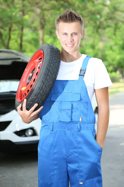 Auto mechanic with tire on his shoulder — Stock Photo, Image