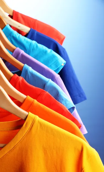 Lots of T-shirts on hangers on blue background — Stock Photo, Image