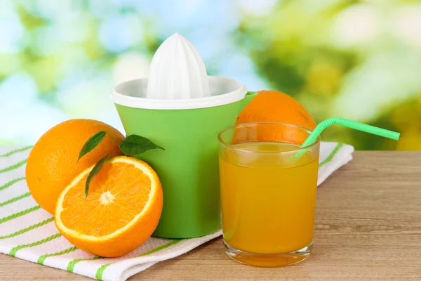 Citrus press, glass of juice and ripe oranges on brown wooden table — Stock Photo, Image