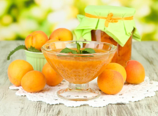 Apricot jam in glass jar and fresh apricots, on wooden table, on bright background — Stock Photo, Image