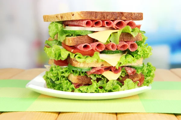 Huge sandwich on wooden table, on bright background — Stock Photo, Image