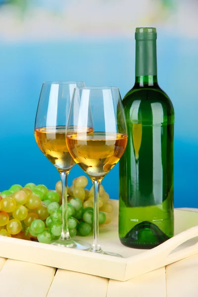 Uvas maduras, garrafa e copos de vinho na bandeja, no fundo brilhante — Fotografia de Stock