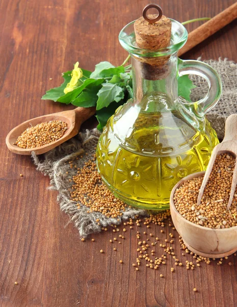 Vaso di olio di senape e semi con fiore di senape su sfondo di legno — Foto Stock