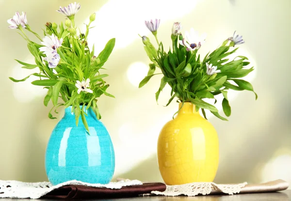Букет красивых летних цветов в цветных вазах, на деревянном столе, на ярком фоне — стоковое фото