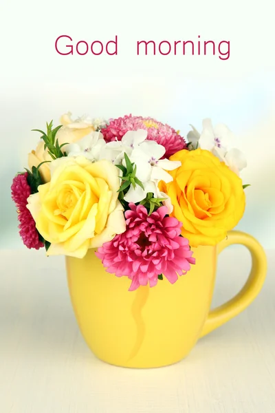 Beautiful bouquet of bright flowers in color mug, on wooden table, on light background — Stock Photo, Image