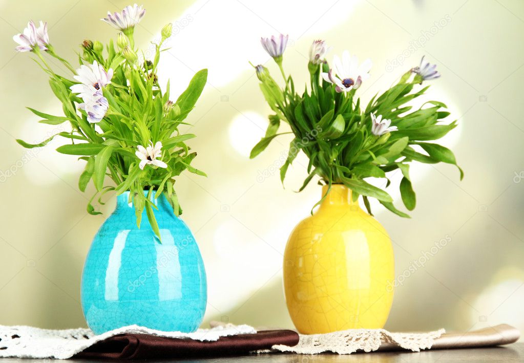 Bouquet of beautiful summer flowers in color vases, on wooden table , on bright background