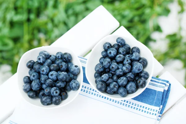 Blåbär i plattor på servett på träbord på gräs bakgrund — Stockfoto