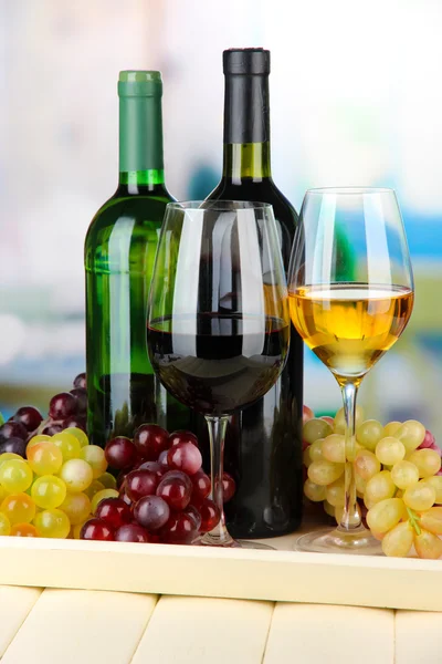 Wine bottles and glasses of wine on tray, on bright background — Stock Photo, Image
