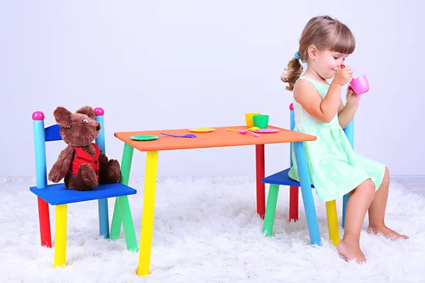 Kleines nettes Mädchen sitzt auf kleinem Stuhl am Tisch, auf grauem Hintergrund — Stockfoto