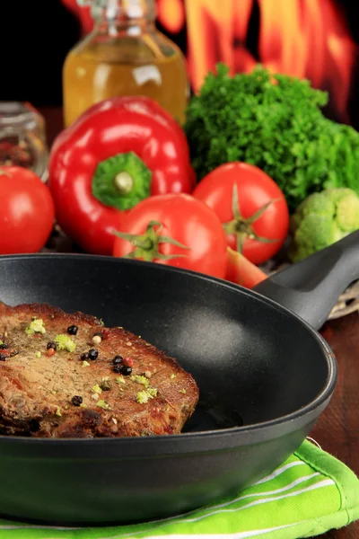 Stekt köttbit på pan på träbord på brand bakgrund — Stockfoto