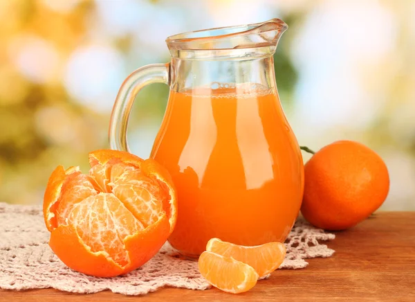 Jarra llena de jugo de mandarina, sobre mesa de madera sobre fondo brillante —  Fotos de Stock