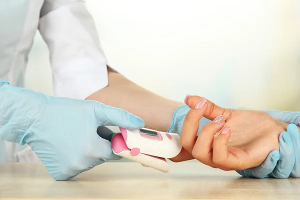 Doctor measuring pulse rate and oxygen levels, on bright background — Stock Photo, Image
