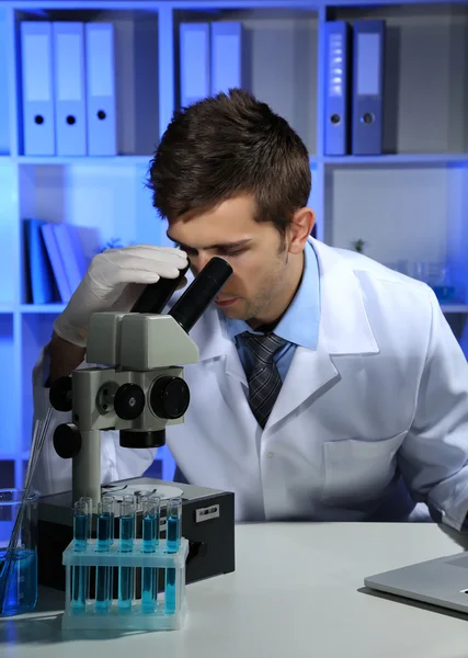 Junge Laborantin betrachtet Mikroskop im Labor — Stockfoto