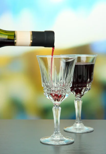 Red wine being poured into wine glass, on bright background — Stock Photo, Image