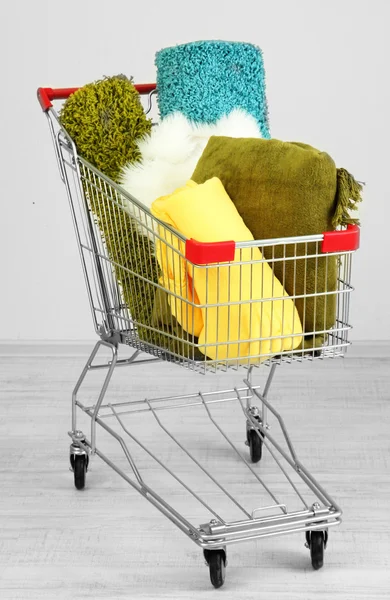 Shopping cart with colorful carpets and plaids, on color wall background — Stock Photo, Image