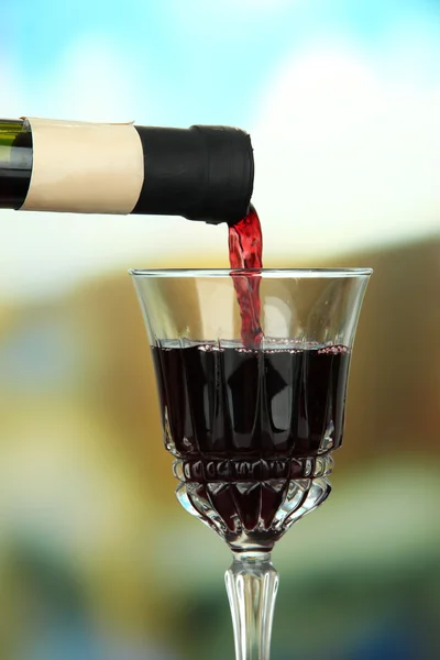 Vinho tinto sendo derramado em copo de vinho, em fundo brilhante — Fotografia de Stock