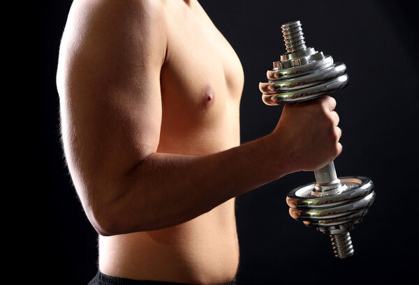 Handsome young muscular sportsman execute exercise with dumbbell on dark background