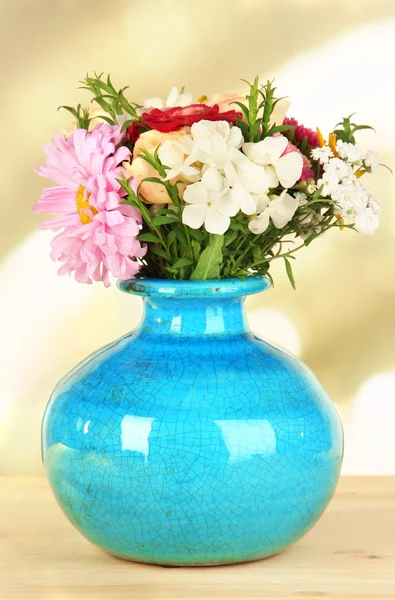Красивый букет ярких цветов в цветной вазе, на деревянном столе, на ярком фоне — стоковое фото