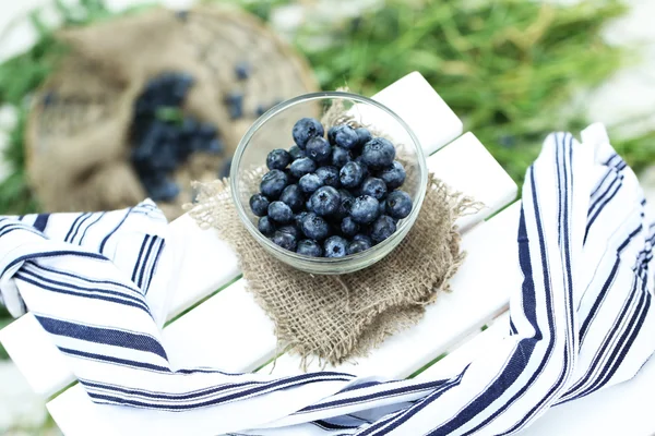 Blueberry di piring kaca dekat serbet di meja kayu pada latar belakang rumput — Stok Foto