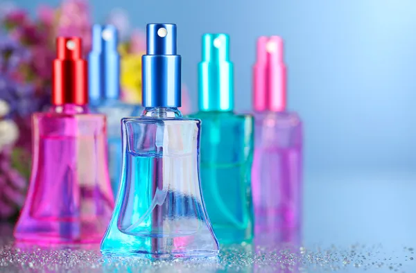 Women perfume in beautiful bottles and flowers on blue background — Stock Photo, Image