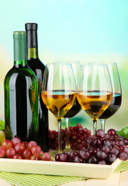 Wine bottles and glasses of wine on tray, on bright background — Stock Photo, Image