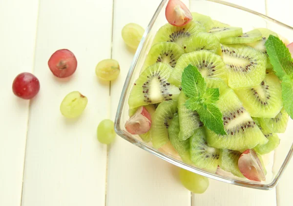 Smakelijke fruitsalade in glazen kom, op witte houten tafel — Stockfoto