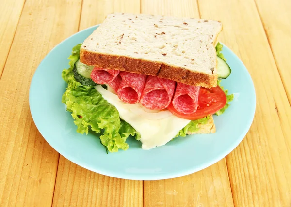 Sanduíche saboroso com salsicha de salame e legumes na placa azul, no fundo de madeira — Fotografia de Stock