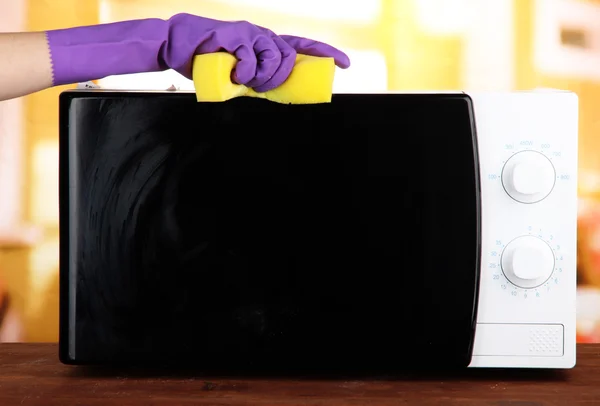 Hand with sponge cleaning microwave oven, on bright background — Stock Photo, Image