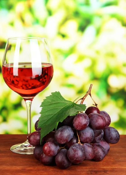 Uvas maduras deliciosas com copo de vinho na mesa em fundo brilhante — Fotografia de Stock