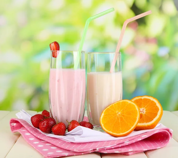 Delicious milk shakes with strawberries and orange on wooden table on natural background — Stock Photo, Image