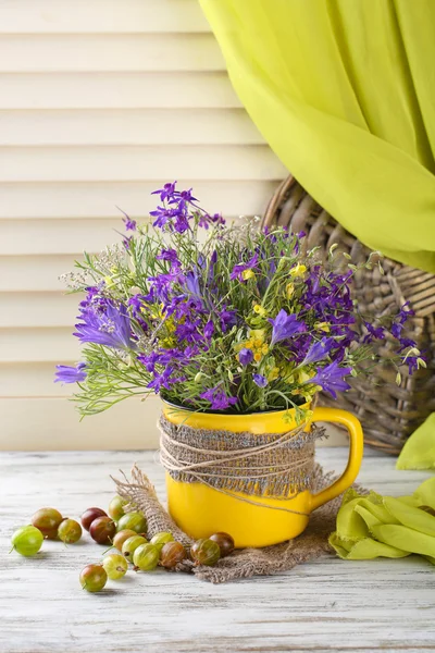 Schöner Strauß Wildblumen in Tasse und Beeren auf Holztisch — Stockfoto