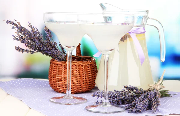 Lavender lemonade in glass jug and cocktail glasses, on bright background — Stock Photo, Image