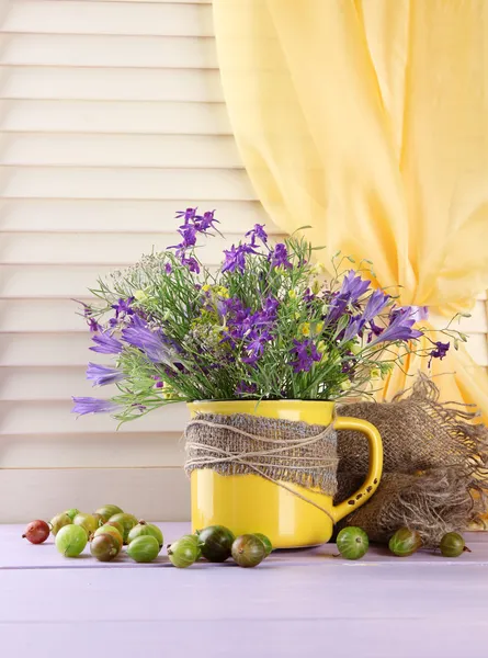 Beautiful bouquet of wildflowers in cup and berries on wooden table — Stock Photo, Image