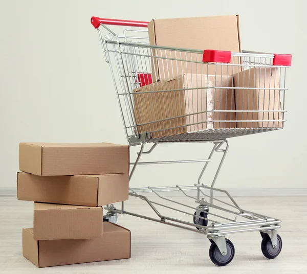 Shopping cart with carton, on gray background — Stock Photo, Image