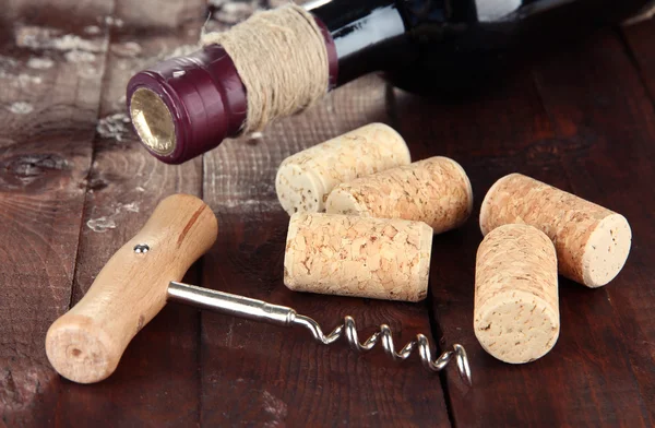 Corkscrew with wine corks and bottle of wine on wooden table close-up — Stock Photo, Image