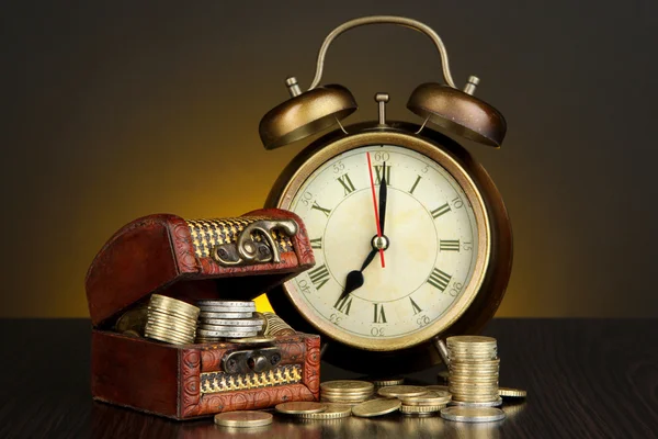 Antieke clock en munten op houten tafel op donkere kleur achtergrond — Stockfoto