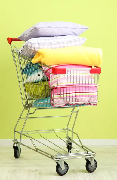 Carrito de compras con almohadas, sobre fondo de pared verde —  Fotos de Stock