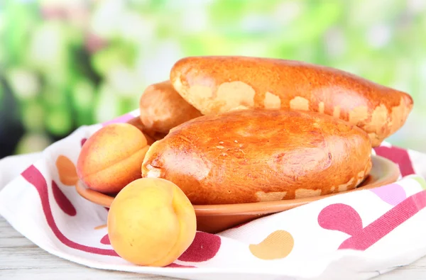 Fresh baked pasties with fruit jam, on wooden table, on bright background — Stock Photo, Image