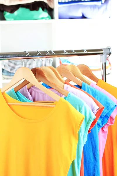 Variety of casual t-shirts on wooden hangers on shelves background — Stock Photo, Image