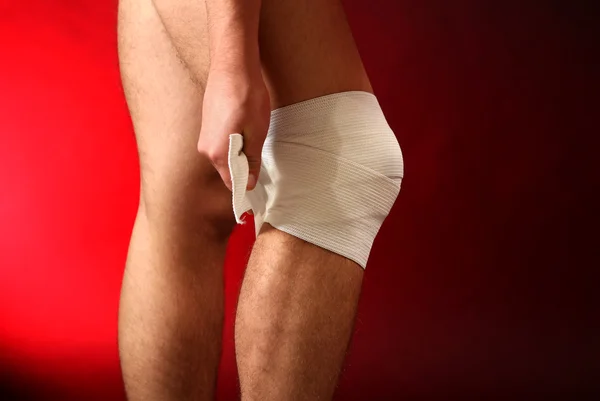 赤い背景上の膝の上に弾性包帯と若い男 — ストック写真