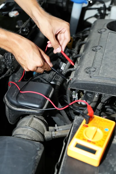 Automechaniker verwendet Multimeter-Voltmeter, um Spannungsniveau in Autobatterie zu überprüfen — Stockfoto